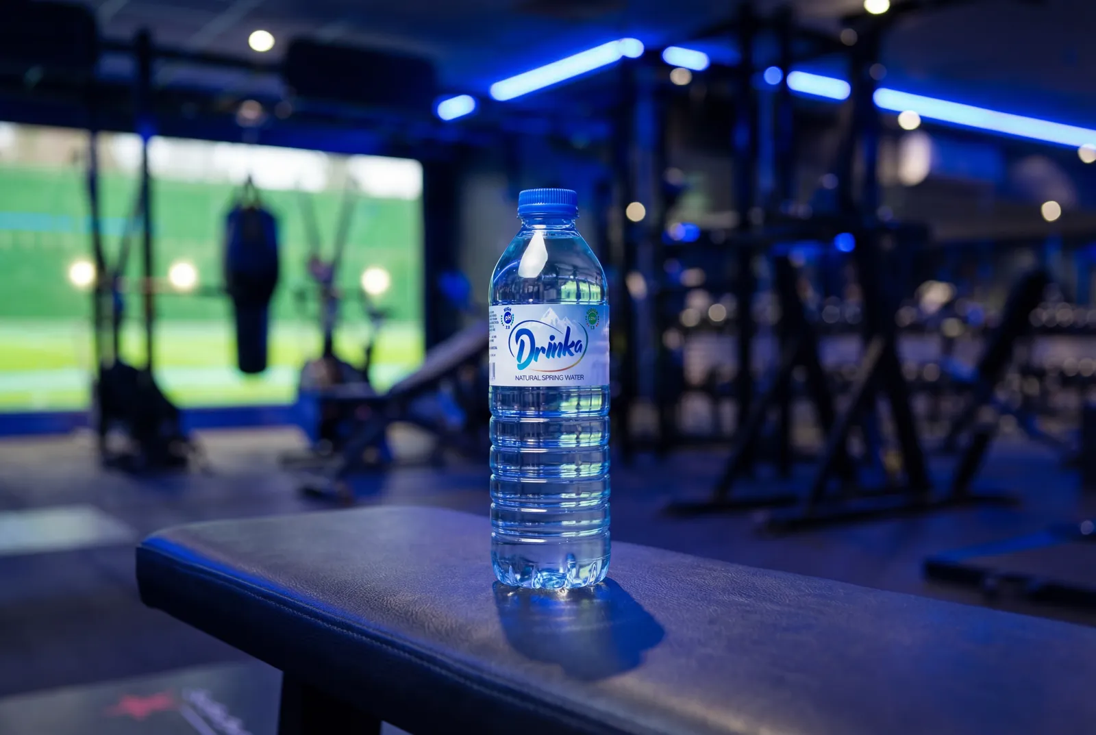 Bottle of Drinka natural spring water on a gym bench beside workout equipment